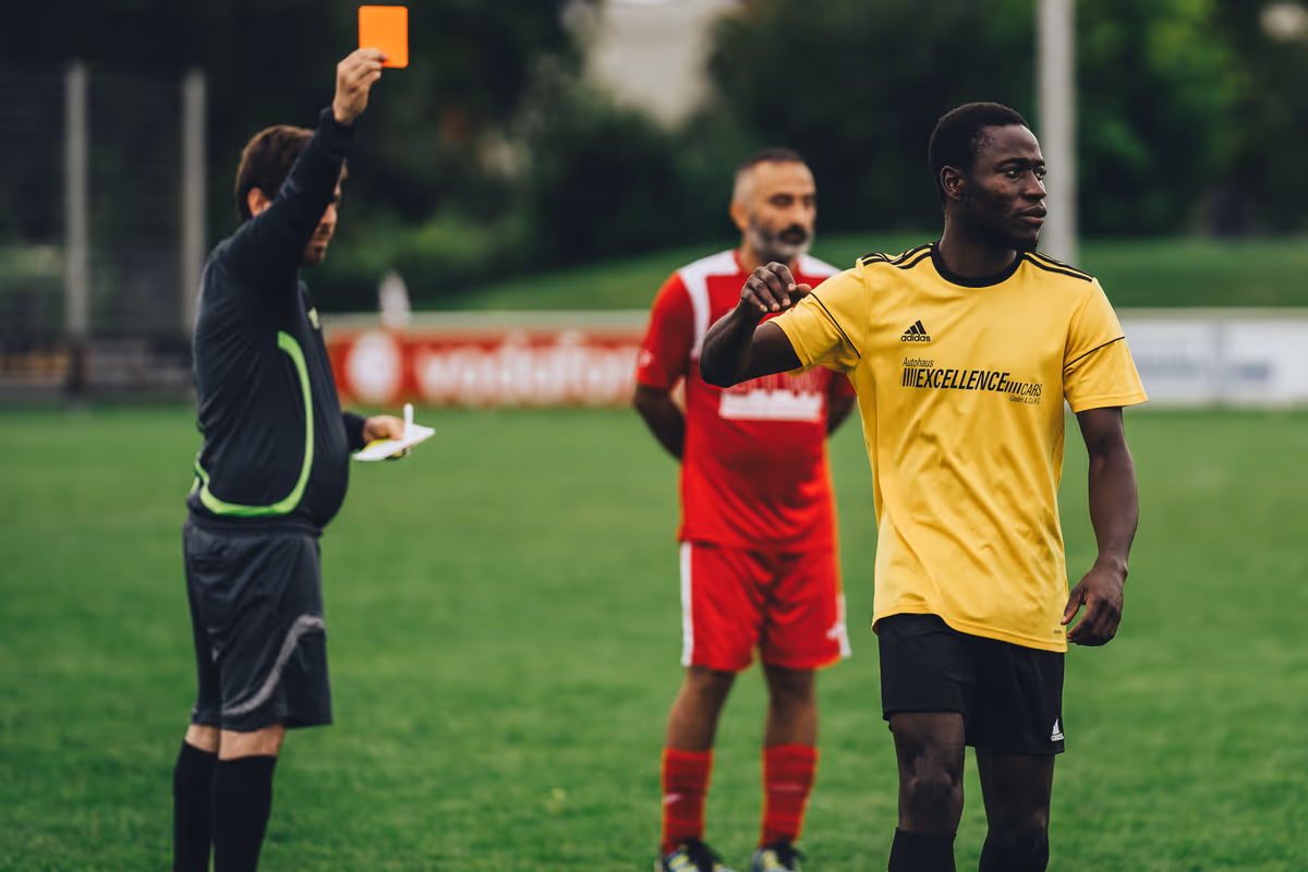 A football referee holding up a red card on the pitch