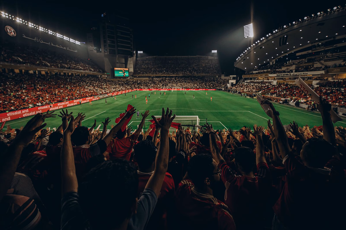 A packed night stadium with fans raising their arms at a major football match