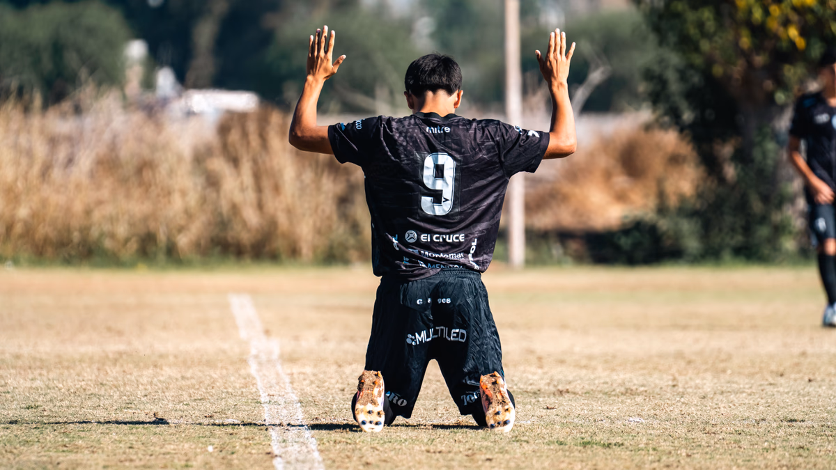 A footballer kneels and raises his arms to celebrate a goal on the pitch