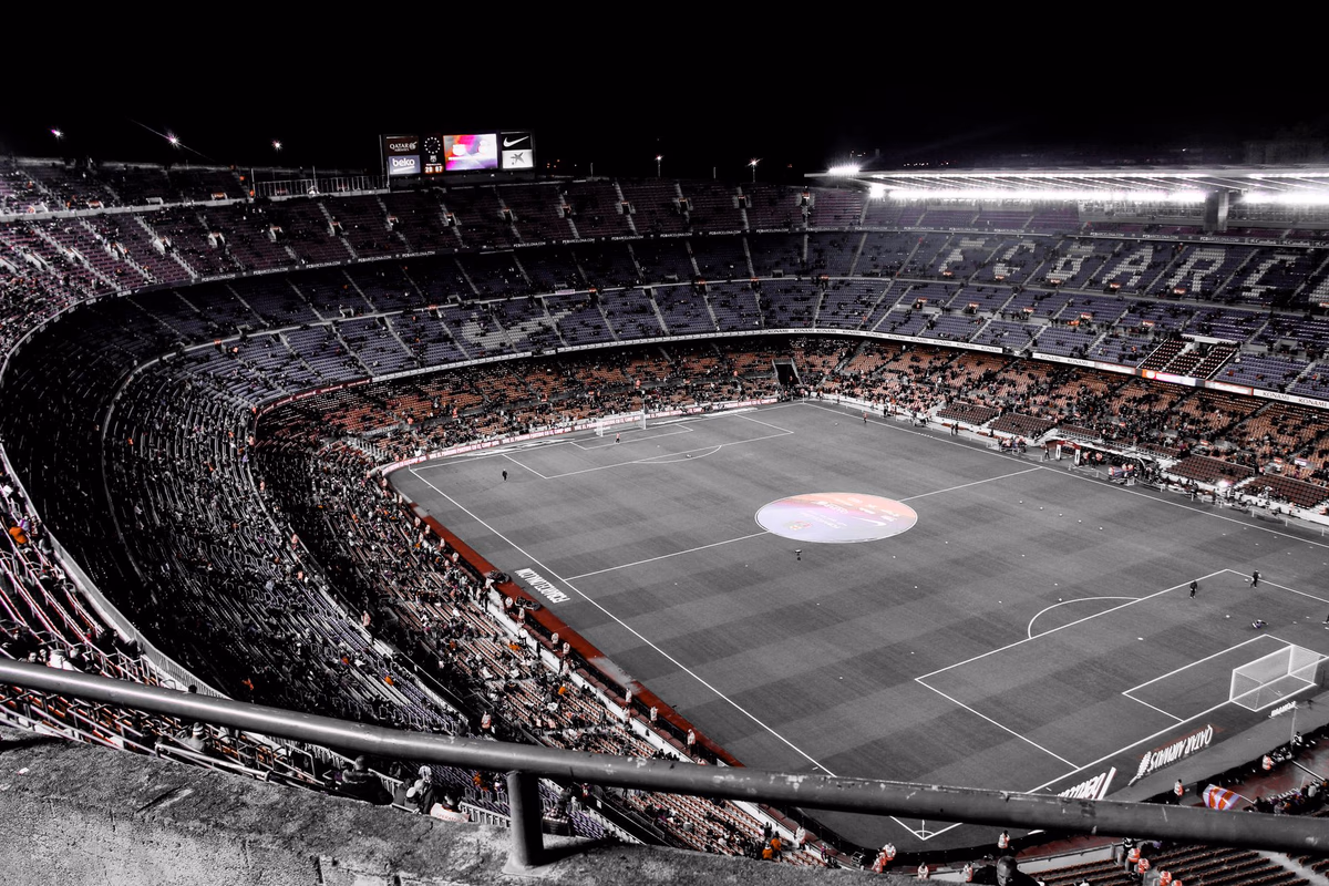 A floodlit football stadium at night, the stands wrapping around the pitch before a big match