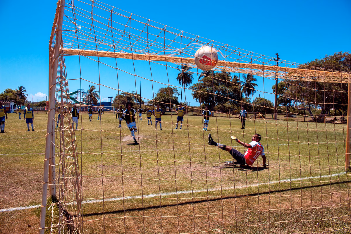 A football crosses the goal line into the net as the goalkeeper falls, beaten, in a daytime match