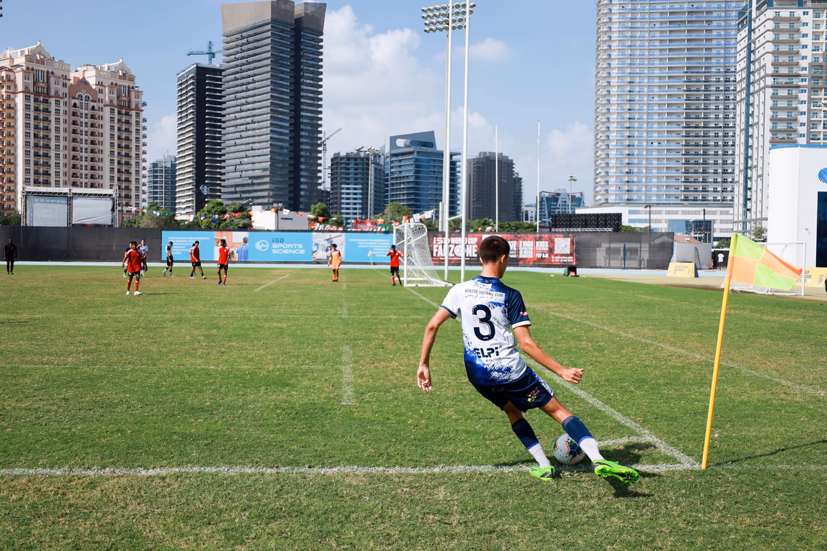 A player prepares to take a corner kick by the corner flag with teammates waiting in the box