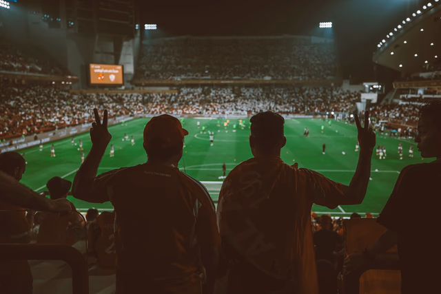 Fans watch the match from the stands in a floodlit stadium at night