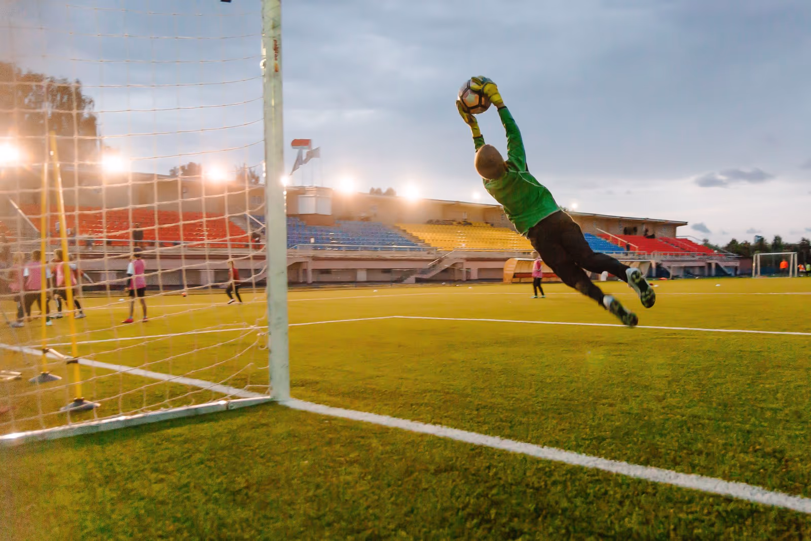 A goalkeeper at full stretch catching the ball in mid-air in front of the goal