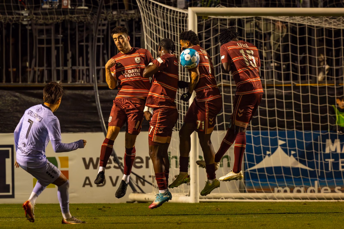 Players jump together in a defensive wall to block a free kick during a night match