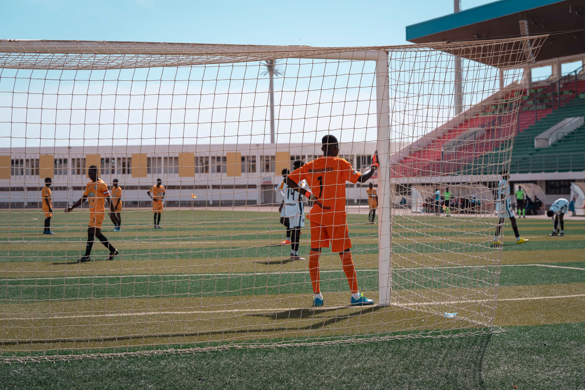 A goalkeeper stands guarding the goal frame, watching play develop further up the pitch