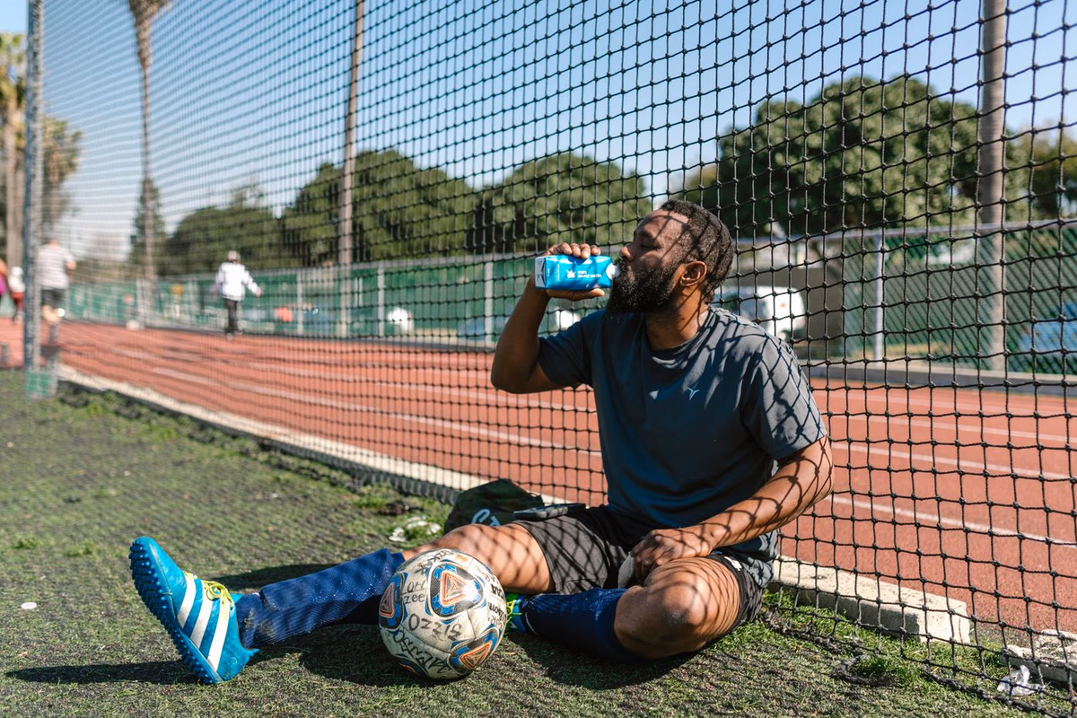 A football player resting and rehydrating beside the pitch after intense effort