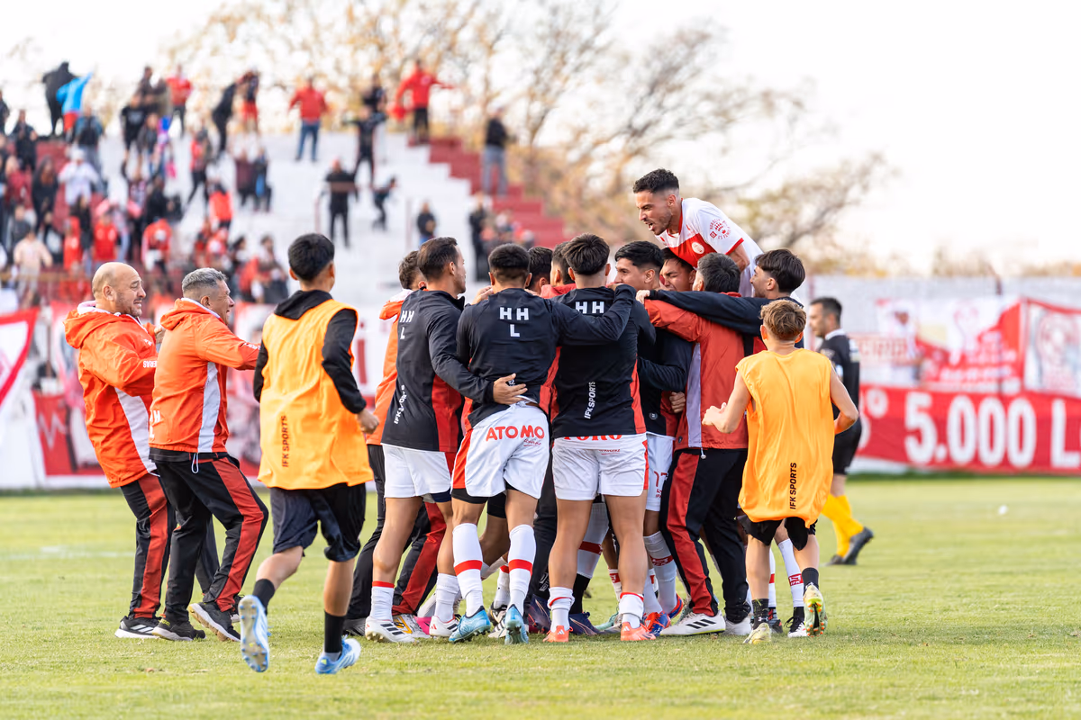 A footballer in home kit celebrating a goal with teammates in front of fans