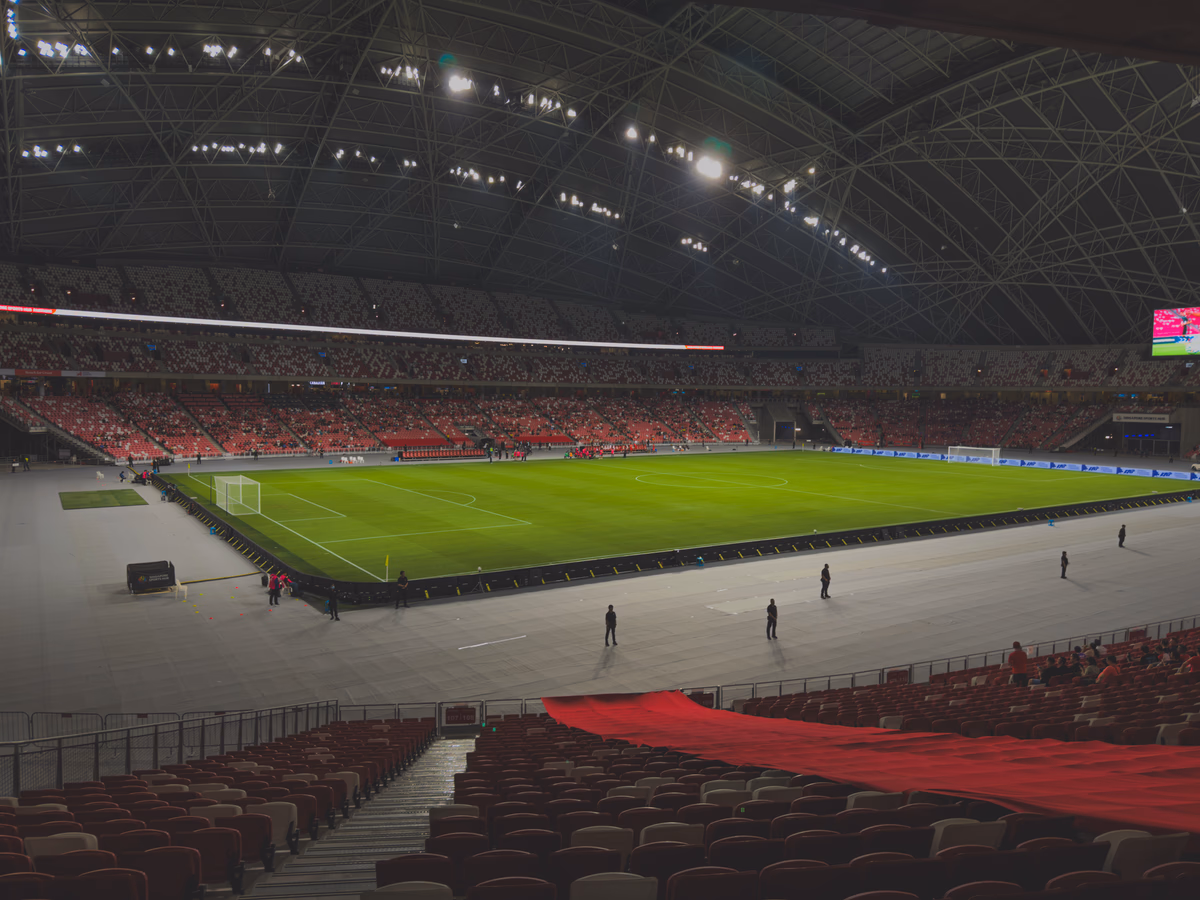 Indoor football stadium with a closed roof and floodlights illuminating the green pitch