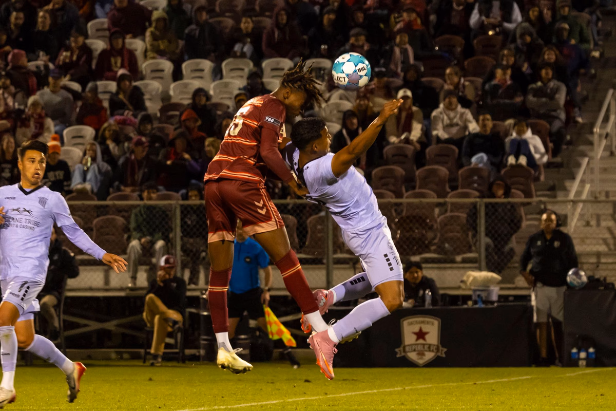 Two footballers jumping to contest a header in mid-air under floodlights during a match