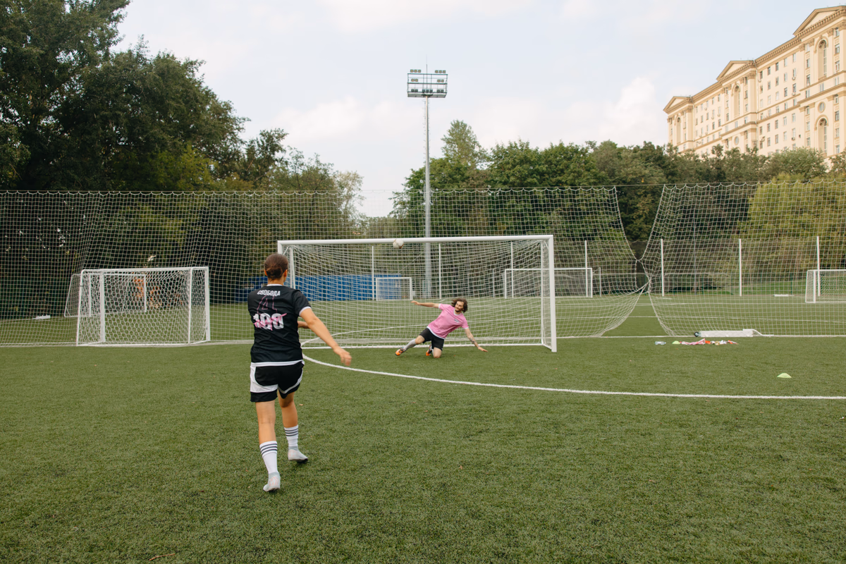 A footballer strikes a shot at goal as the goalkeeper dives to make a save