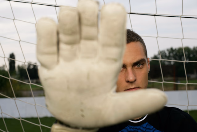 A goalkeeper's glove stretches up to block a shot in close-up during a match