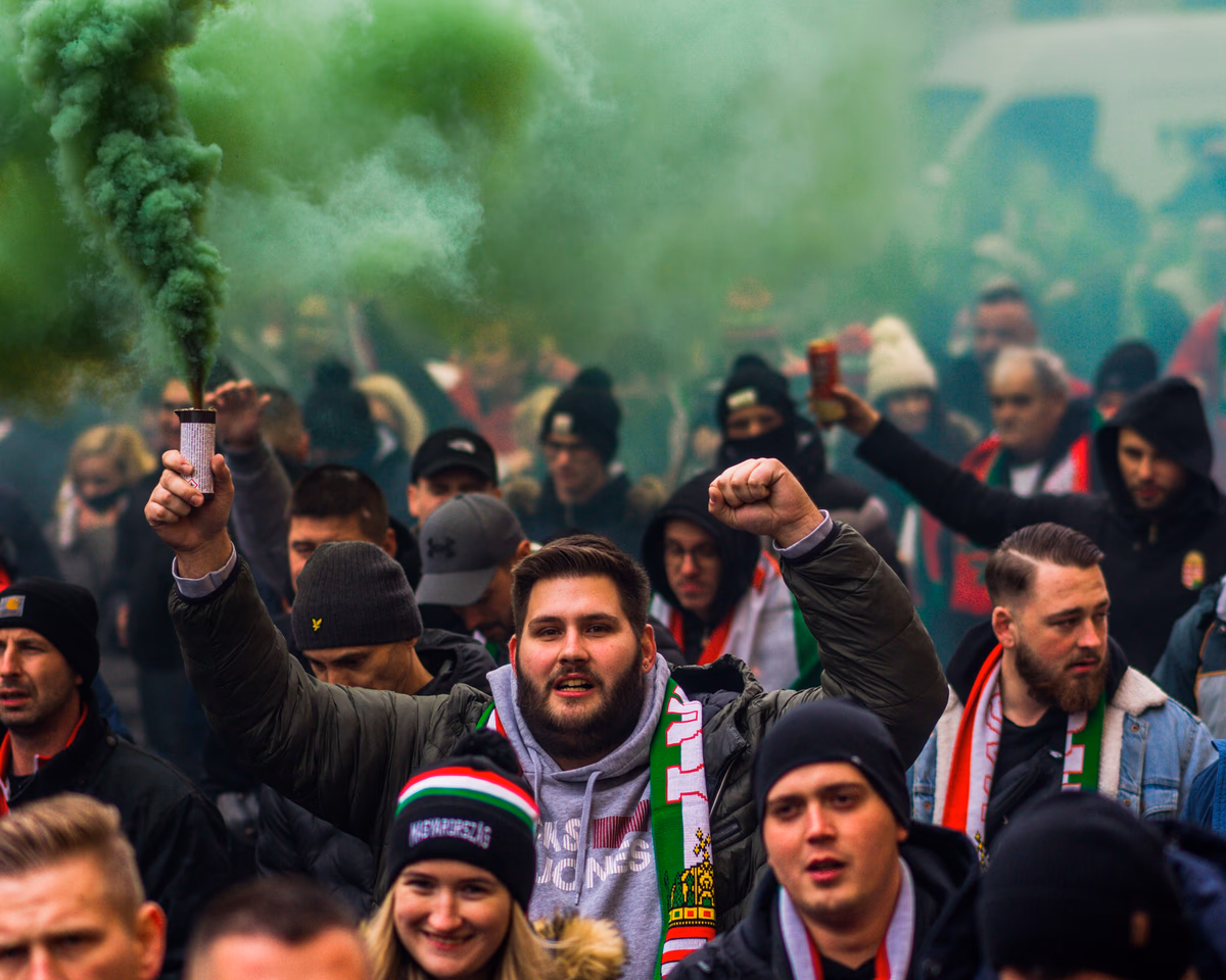 A vibrant crowd of football fans celebrating with smoke flares in a charged match atmosphere