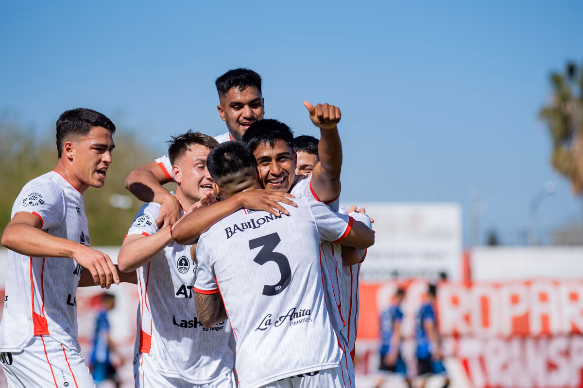 A full football team rushing in to embrace and celebrate a goal together on the pitch