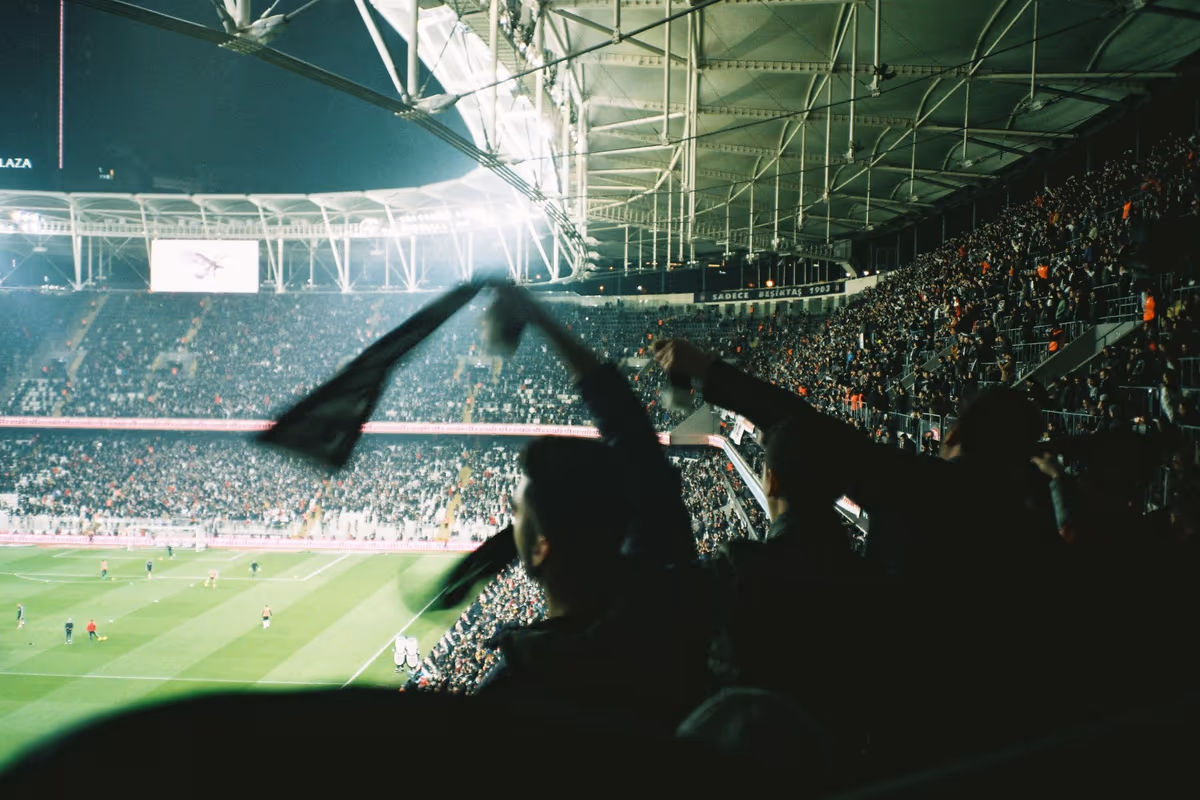 Fans in the stands waving scarves and cheering their team at a night football match