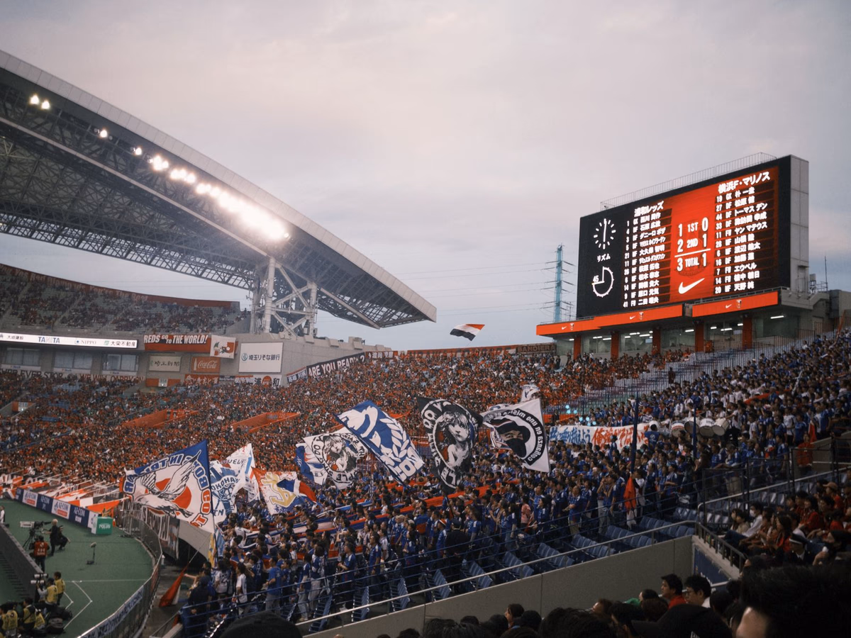 A packed crowd of Asian football fans waving flags and banners in a stadium