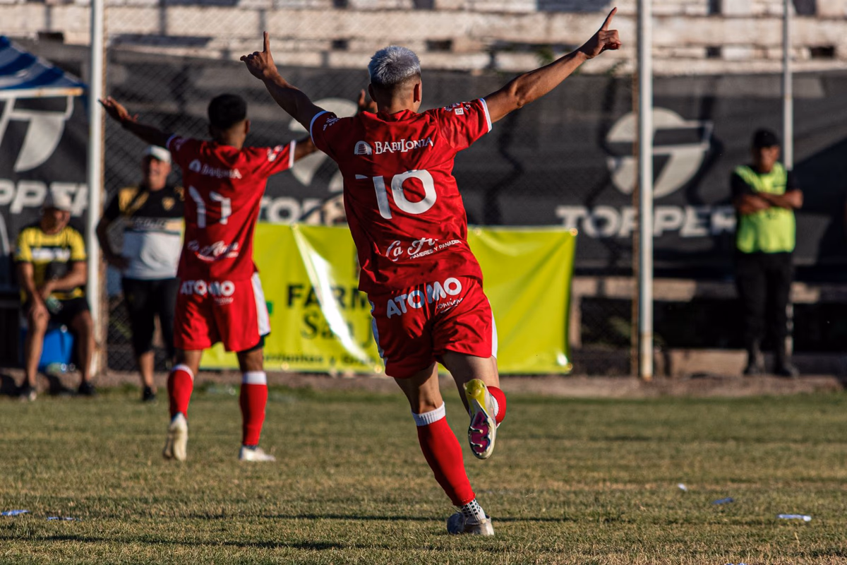 A footballer in a red number 10 shirt raising his arms to celebrate a goal