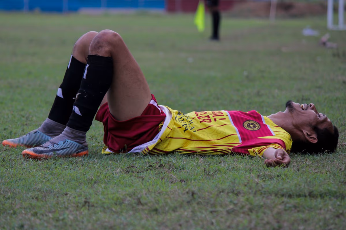 A footballer lying exhausted on the pitch after a hard match