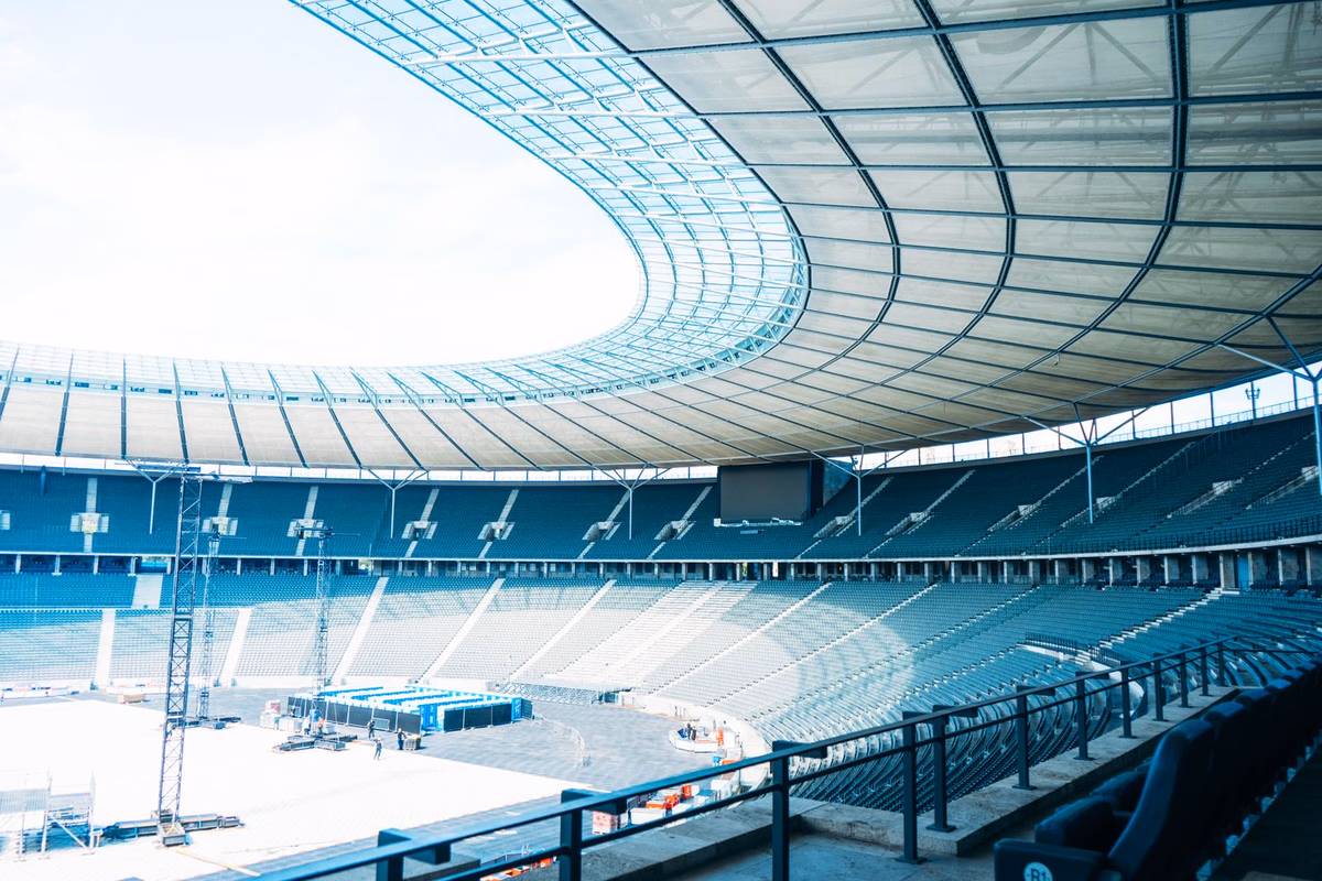 A large curved roof structure over the empty stands of a football stadium