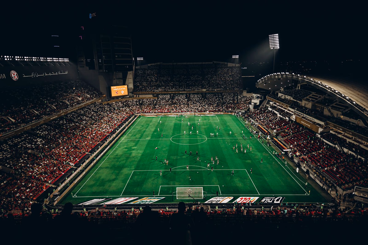 A packed football stadium bowl at night under floodlights